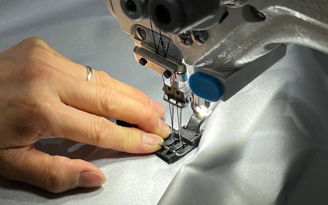 A close-up of a factory worker's hands operating a sewing machine on a piece of fabric